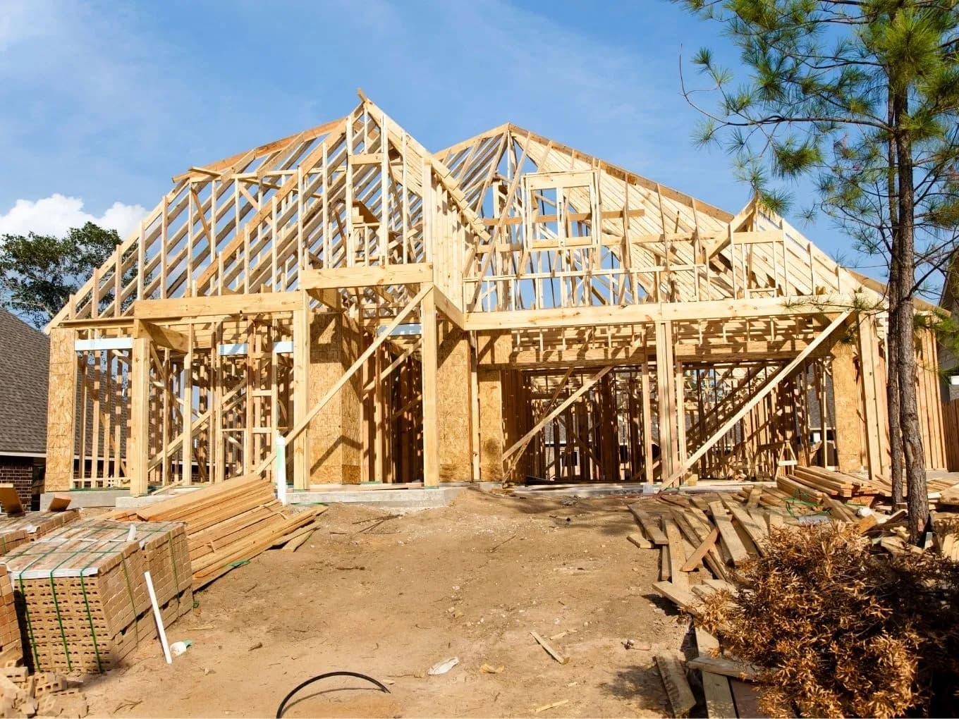 The consturction phase of a new house, wood beams and stacks of wood on top of a clear dirt foundation.