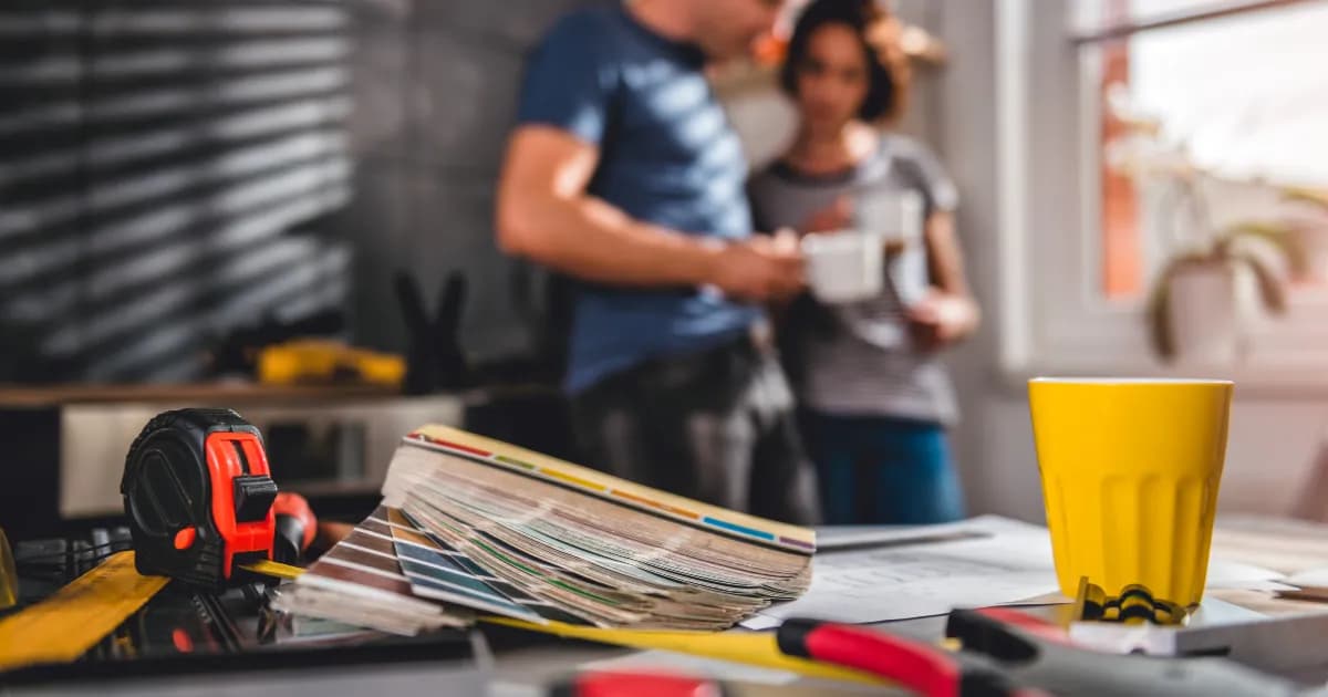 Two people sipping coffee and choosing paint colors in a house undergoing a renovation.