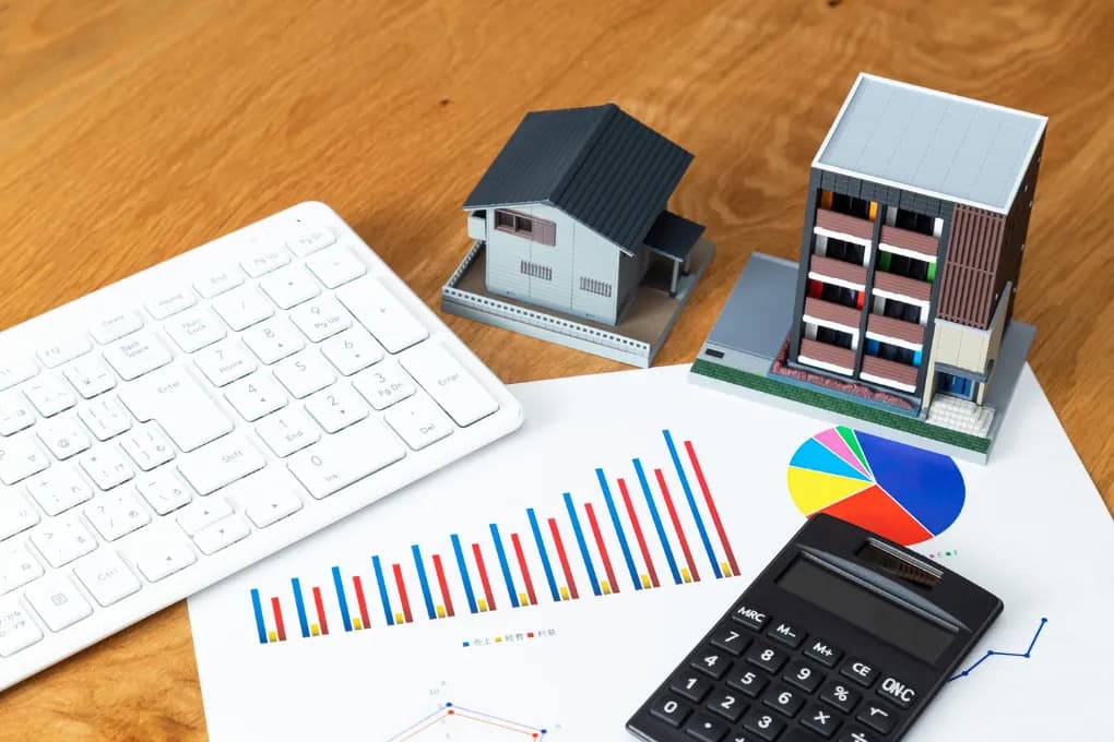 image of spreadsheets, computer keyboard and toy multifamily house